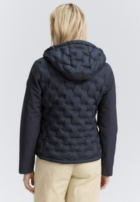 Giubbotto imbottito navy con motivo trapuntato nella parte superiore, maniche lisce e cappuccio. Tessuto leggero e design aderente.