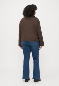 Brown textured jacket with a relaxed fit, paired with flared blue jeans. The jacket has a collar and long sleeves. Black heeled boots are worn.