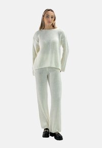 Ribbat stickad tröja och matchande byxor i off-white, med avslappnad passform, långa ärmar och strukturert tyg. Svarta chunky skor som fotbeklädnad.