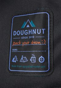 Czarna naszywka z materiału z niebieskim i pomarańczowym napisem. Zawiera logo górskie, "DOUGHNUT od 2010 roku", motywującą frazę i symbole pielęgnacji.