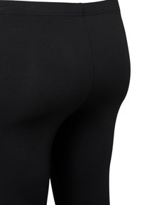 Mustat legginsit, jotka on valmistettu joustavasta kankaasta ja joissa on sileä rakenne ja kiinteä muotoilu. Niissä on yksinkertainen vyötärö ja ei näkyviä kuoseja.