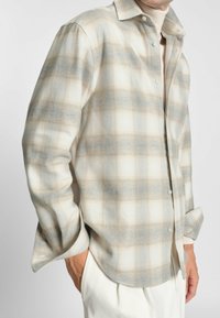 Camicia a maniche lunghe a quadri nei toni crema, blu e beige; tessuto morbido; presenta un design con bottoni e colletto visibile con una vestibilità rilassata.