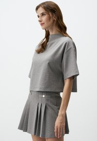 Szary w paski crop top z teksturowanej tkaniny, zestawiony z plisowaną spódnicą z guzikiem z przodu, ukazującą skoordynowany design.