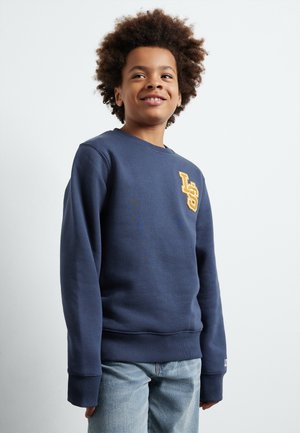 Felpa blu navy in misto cotone con polsini a coste. Caratterizzata da un logo 'LS' giallo cucito sul petto. Abbinata a jeans blu chiaro.