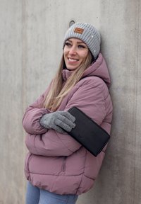Black leather wallet held against a light purple puffer jacket. Grey knit beanie and matching gloves complete the outdoor attire.