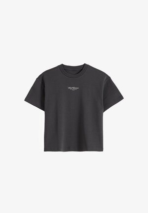 Svart T-skjorte med korte ermer og rund hals, med liten hvit kursiv tekst midt på brystet.