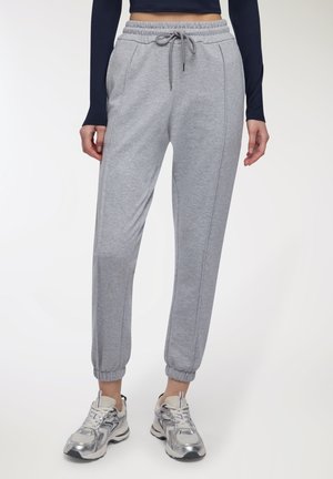 Persona che indossa pantaloni jogger grigi chiari con cintura elastica e cordino, abbinati a scarpe da ginnastica argentate e bianche.