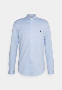 Vaaleansinine pitkähihainen paita, joka on valmistettu kudotusta kankaasta. Paidassa on nappikaulus, etunappit ja pieni tummansininen logo rinnassa.