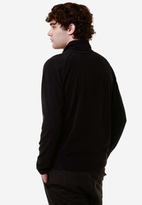 Felpa nera in pile con collo alto e maniche lunghe. Presenta una vestibilità morbida e una texture soffice, che arriva fino alla vita.