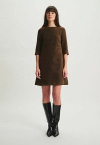 Robe de shift texturée marron avec des manches trois-quarts, un col large et un ourlet évasé. Assortie à des bottes noires élégantes arrivant jusqu'aux genoux.