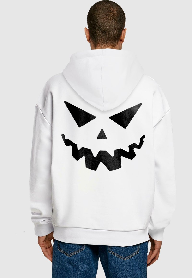 Vit hoodie med en stor svart grafisk bild av ett tandigt leende med triangulära ögon på baksidan. Mjukt tyg, avslappnad passform.