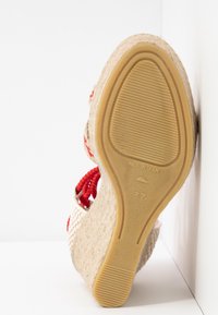 Semelle d'une sandale compensée beige avec des lacets rouges, semelle en caoutchouc texturée marquée "Made in Spain" et taille 37.
