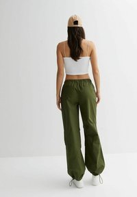 Zelené volné kalhoty s elastickým pasem, bočními kapsami a stahovacími manžetami, doplněné bílým krátkým topem a béžovou čepicí.