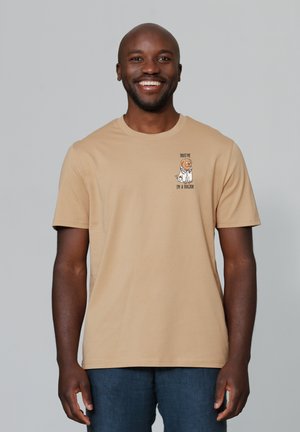 Tan kortärmige T-shirt gemaakt van katoen met een cartoon hond in een laboratoriumjas en de tekst: "Vertrouw me, ik ben een dokter" op de linkerborst.