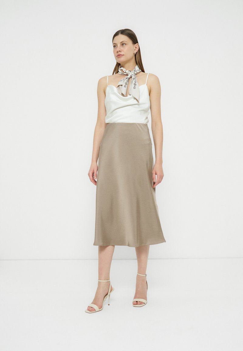 Stylish woman in a satin summer dress for women with a cowl neck and a beige skirt, perfect for sunny days.