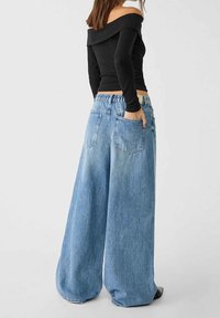 Jeans in denim blu a gamba larga, con una vestibilità rilassata, tessuto morbido e vita elastica; abbinati a un top nero a spalle scoperte.