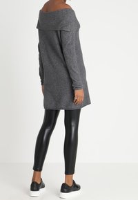 Grau off-shoulder Tunika mit langen Ärmeln und lockerer Passform, kombiniert mit schwarzen Lederleggings und schwarzen Slipschuhen. Glatte Textur.