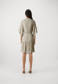 Beige Kleid mit kurzen Ärmeln, strukturiertem Muster, tailliertem Schnitt und Rüschensaum, kombiniert mit weißen Riemchen-Heels.