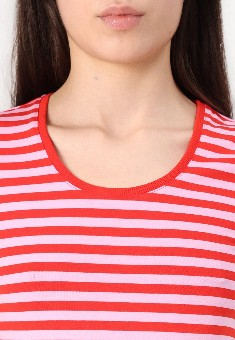 T-shirt rayé rouge et rose avec un col rond, fabriqué en tissu doux, comportant des rayures horizontales de largeurs variées et un col côtelé.
