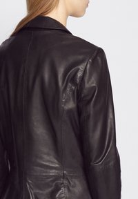Schwarze Lederjacke mit maßgeschneidertem Design, mit Reverskragen, glatter Textur und minimalistischer Naht auf dem Rücken.
