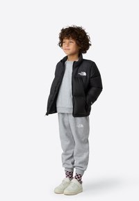 Svart vattert jakke med logo, grå hettegenser, grå joggebukse og hvite joggesko, med rutete sokker. Passer til hverdagsbruk.