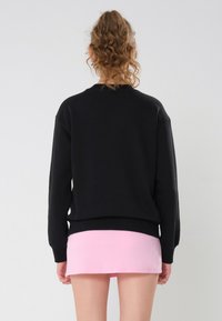 Svart hettegenser med avslappet passform, ribbestrikkede mansjetter og hem. Sammen med et lyse rosa miniskjørt. Teksturen ser myk og uformell ut.
