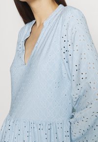 Abito blu chiaro con motivi ricamati e dettagli in pizzo, caratterizzato da scollo a V, maniche lunghe e orlo arricciato.