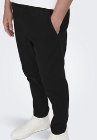 Svarta byxor med elastisk midja, sidfickor och smal passform. I kombination med vita högtoppsneakers.