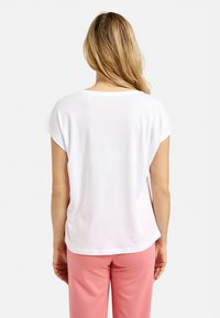 White short-sleeve top with a relaxed fit, round neckline, and smooth texture, paired with light pink pants.