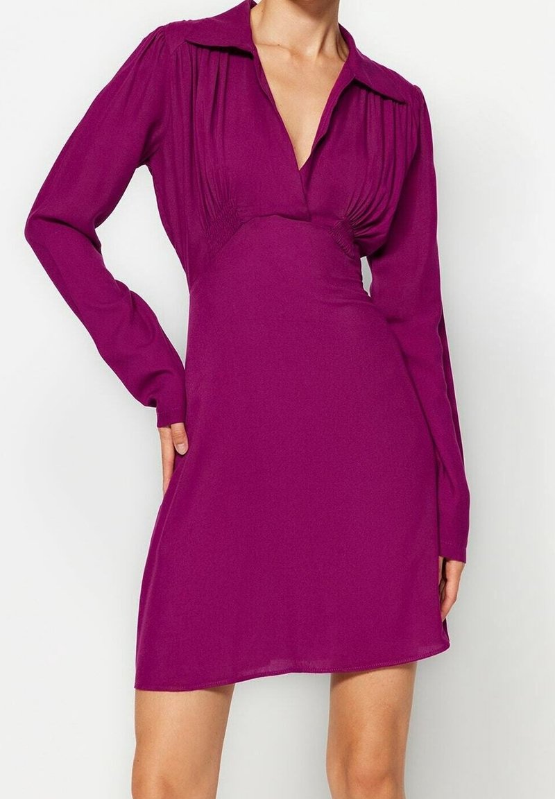 Åtsittande långärmad klänning i livlig lila tyg. Har en krage, plisserad bystdetalj och en något utsvängd kjol.