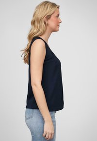 Haut sans manches bleu marine avec une coupe décontractée et des accents en dentelle aux épaules, associé à un jean en denim bleu clair. Texture lisse et design simple.