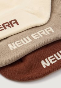 Trīs zeķu pāri krēmkrāsā, gaiši brūnā un tumši brūnā krāsā. Katras zeķes dizainā ir "NEW ERA" logo kontrastējošā tekstā. Mīksts adījums, struktūras virsma.