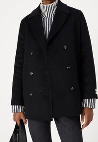 Zwarte wollen peacoat met een dubbelgebreid ontwerp, een notch-kraag en zwarte knopen. Daaronder een geribbelde trui met witte en marineblauwe strepen.