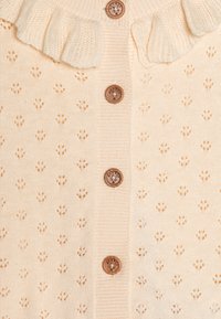 Cardigan lavorato a maglia di colore crema chiaro con colletto arricciato, caratterizzato da modelli decorativi a occhio di pernice e cinque bottoni marroni sul davanti.