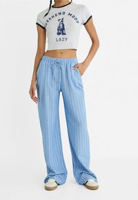 Szary crop top z grafiką kota i napisem "WEEKEND MOOD LAZY"; niebieskie szerokie spodnie w paski z elastycznym pasem i sznurkiem.