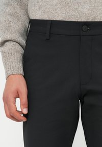 Černé kalhoty z hladké látky s fitted střihem, s předním zapínáním na knoflík, poutky na pásek a plochým předním dílem.
