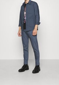 Blå tvådelad outfit med en jacka som har krage och fickor, i kombination med tajta byxor. Bärs med svarta stövlar.