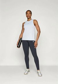 Světle modrý bezrukávový top a tmavě šedé legíny, s černou láhví na vodu v ruce; elegantní sportovní design, přiléhavý střih, lehký materiál.