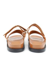 Bruine leren sandalen met platte zwarte zolen, voorzien van twee verstelbare banden en een gladde, getextureerde inlegzool. De achteraanzicht toont het ontwerp.