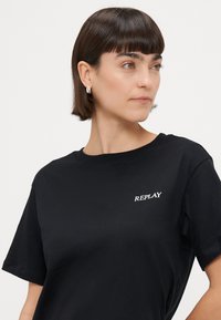 Fekete pamut póló kerek nyakkal és rövid ujjakkal. Elején fehér "REPLAY" logóval. Sima tapintású, laza fazonnal.