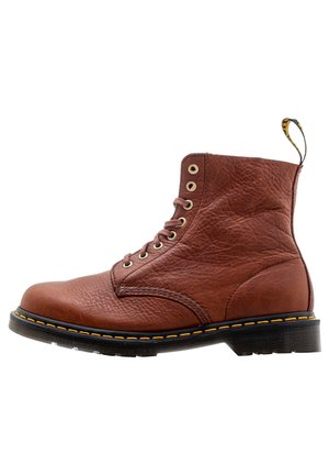 Brauner Leder-Schnürstiefel mit schwarzer Sohle, gelber Naht und Zuglasche hinten, im Profil dargestellt.