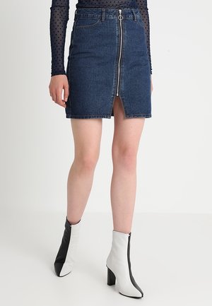 Gonna di jeans a mini lunghezza con zip anteriore e spacco frontale, caratterizzata da un orlo grezzo. Indossata con stivali alla caviglia bianchi e neri con tacco alto.