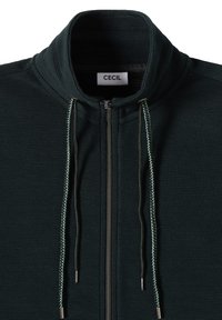 Tmavě zelená bunda na zip s texturovanou tkaninou, vysokým límcem a kontrastními šnůrkami. Obsahuje stříbrný zip a značkovou etiketu.