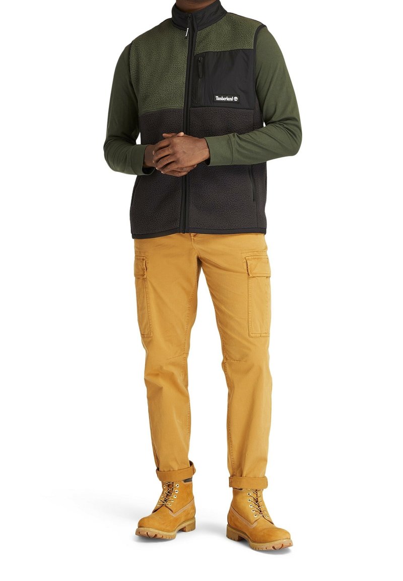 Fleeceväst i mörkgrön och svart, dragkedja fram, en bröstficka. Kombinerad med senapsgula cargobyxor och tanfärgade kängor med snörning.