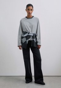 Camisa de manga larga a rayas con cuello redondo, combinada con pantalones anchos negros. Un suéter gris con patrón de rombos atado a la cintura agrega textura.