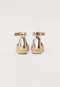 Metallische gouden espadrille sandalen met enkelbandje en geweven jute zool. Open achterontwerp met een gladde textuur en minimale details.
