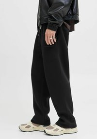 Schwarze weit geschnittene Hosen aus weichem Stoff, mit einer Seitentasche und elastischem Bund, kombiniert mit cremefarbenen Sneakers und silbernen Ringen.