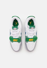 Valkoiset lenkkitossut harmailla yksityiskohdilla, vihreällä hihnalla ja keltaisella "NIKE"-tekstillä. Kenkä on varustettu pyöreillä rei'illä ja vihreällä pohjallisella, jossa on logo.