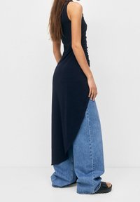 Vestido sin mangas de color marino con detalles fruncidos, combinado con pantalones de mezclilla grandes de color azul claro. Sandalias con tiras negras texturizadas completan el conjunto.