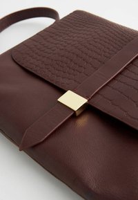 Sac à main en cuir bordeaux avec texture reptilienne sur le rabat ; doté d'une fermeture à boucle carrée en métal doré et d'une sangle mince et ajustable.